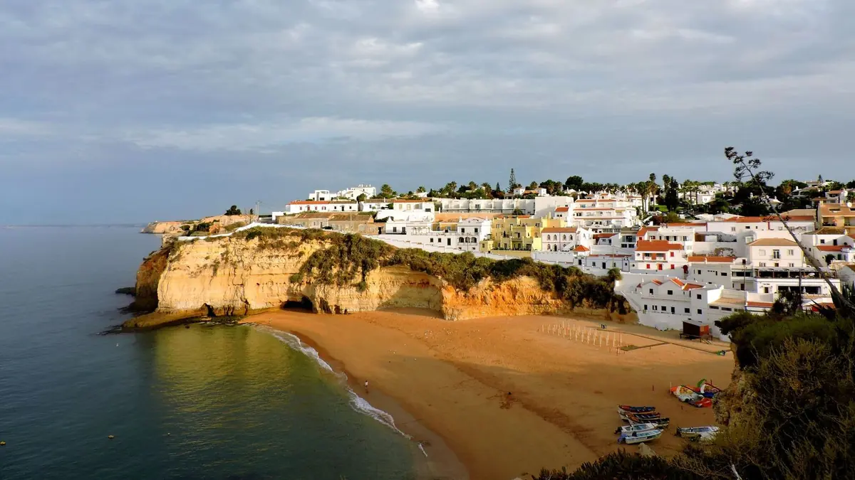 The golden beach of Carvoeiro below limestone cliffs, with the white houses of the village climbing the hill and fishing boats on the sand