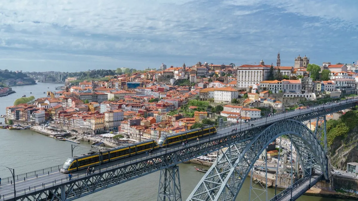 Metro trains crossing the iron Dom Luís I bridge over the Douro, with the colourful houses and churches of Porto's Ribeira quarter behind